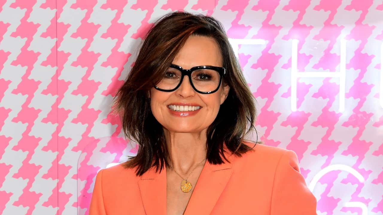 A woman in black glasses and an orange blazer