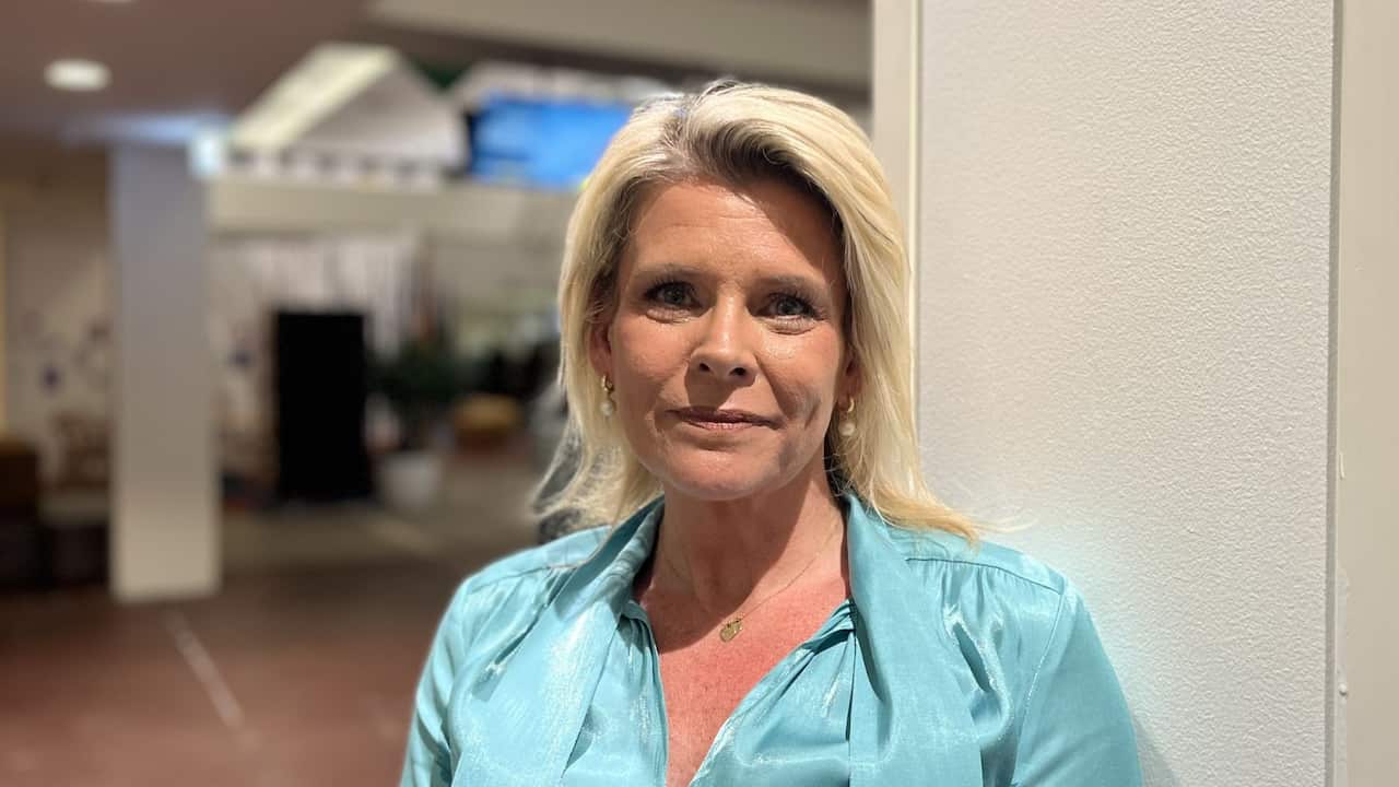 a blonde woman in a light blue blouse smiles in an office