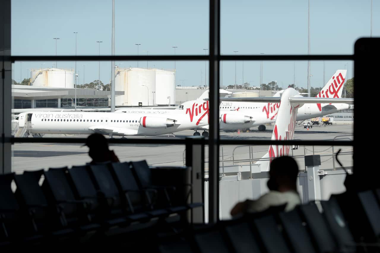 Silhouettes of two peopel sitting on seats at an airport. There are Virgin planes outside on the tarmac.