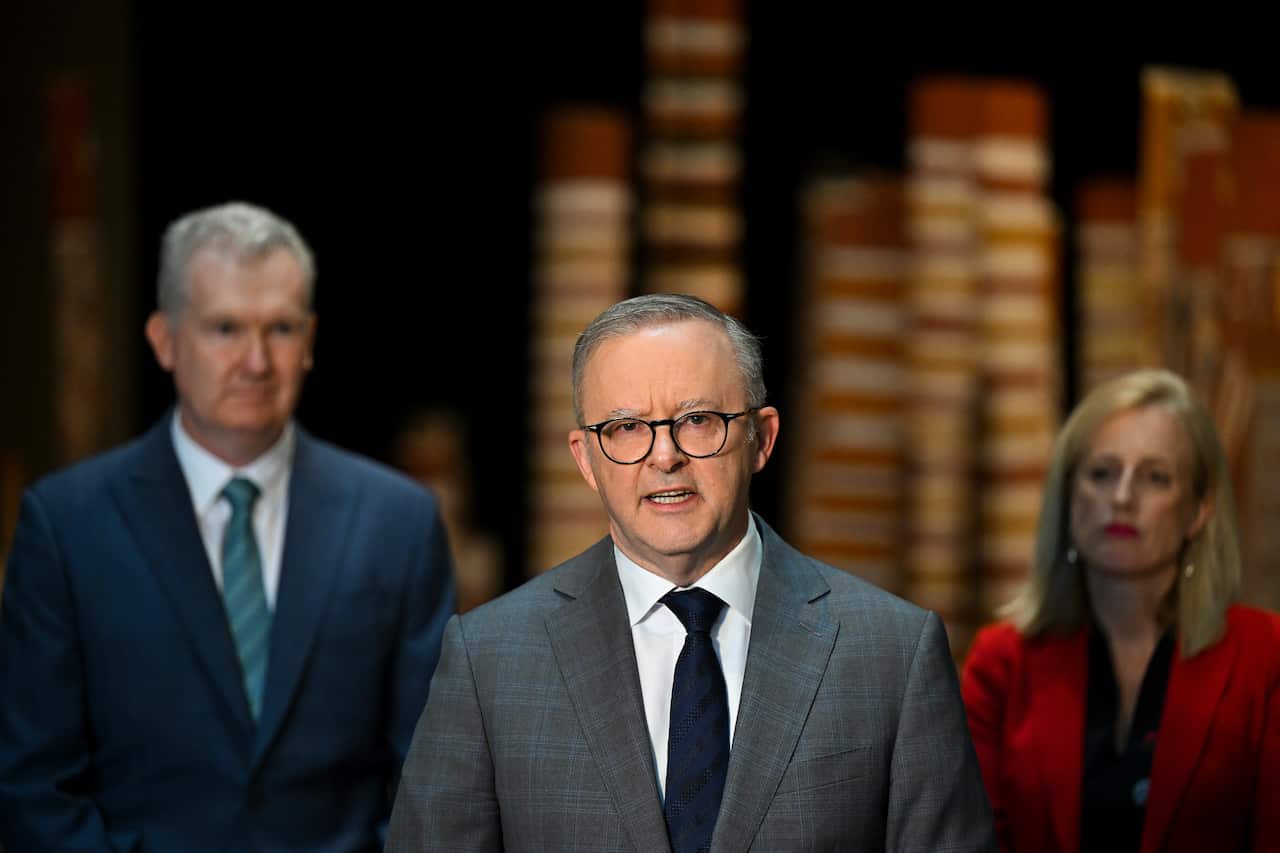 Man in suit and tie speaking in front of two colleagues.