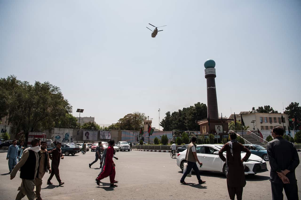A helicopter in the sky as people watch from below.