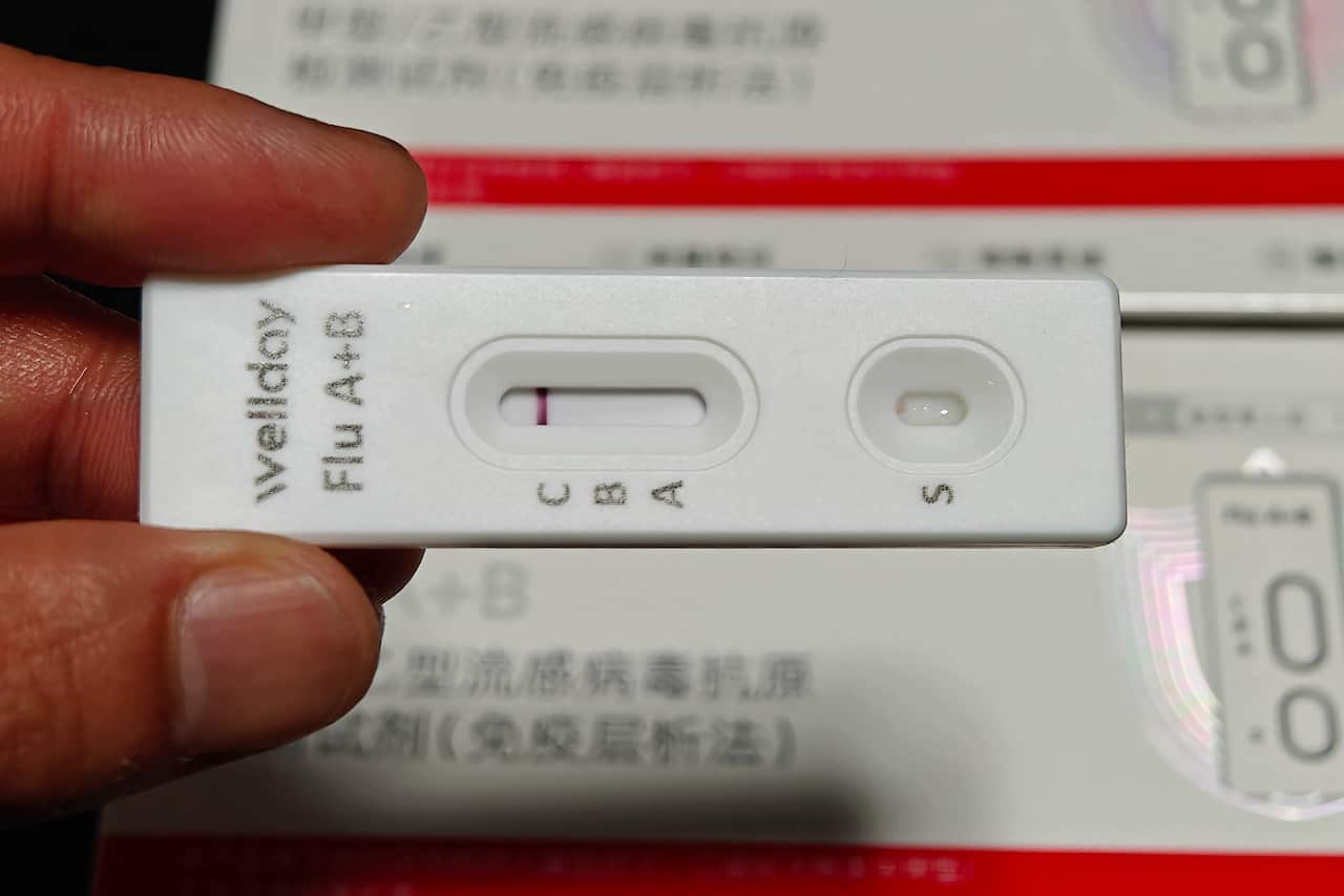 Fingers holding up a rapid antigen test with display areas for influenza A and B.