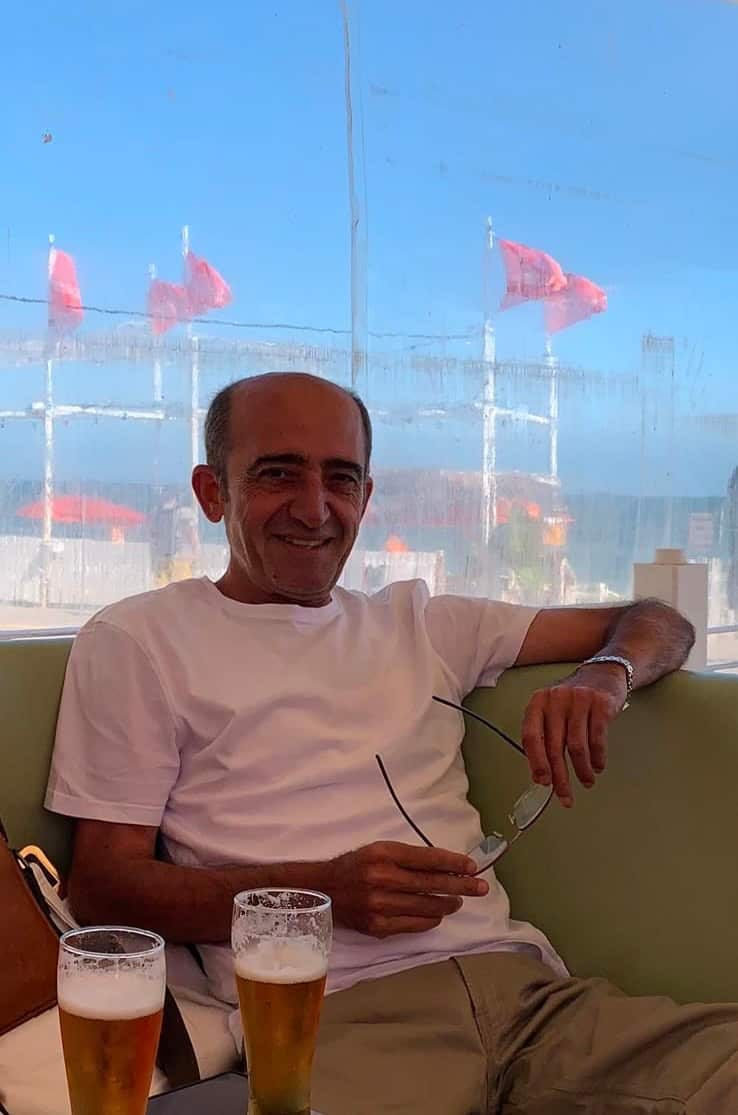 A man wearing a white shirt and holding glasses.