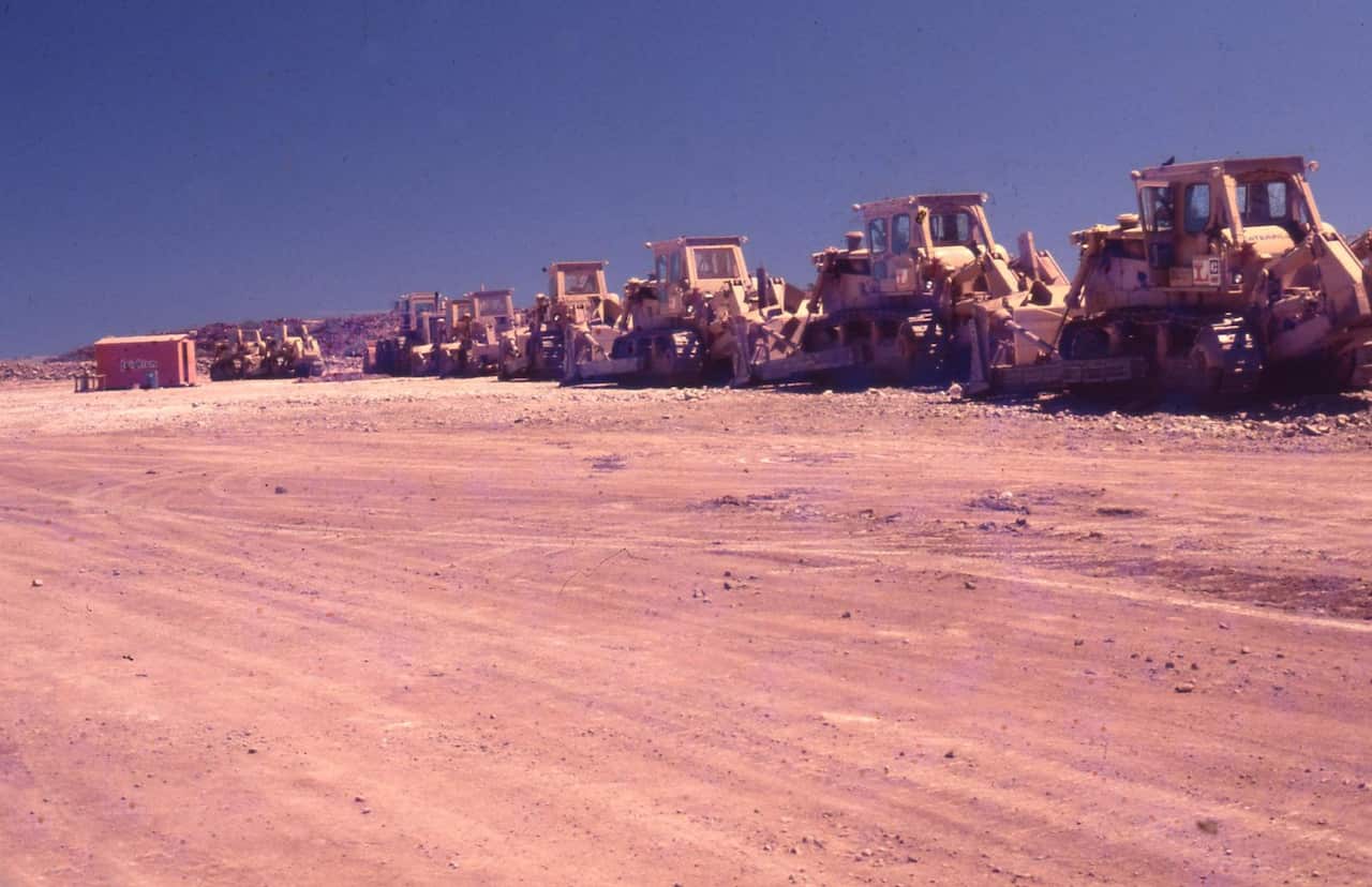 A long line of heavy bulldozers and earthmoving machinery parked side-by-side.