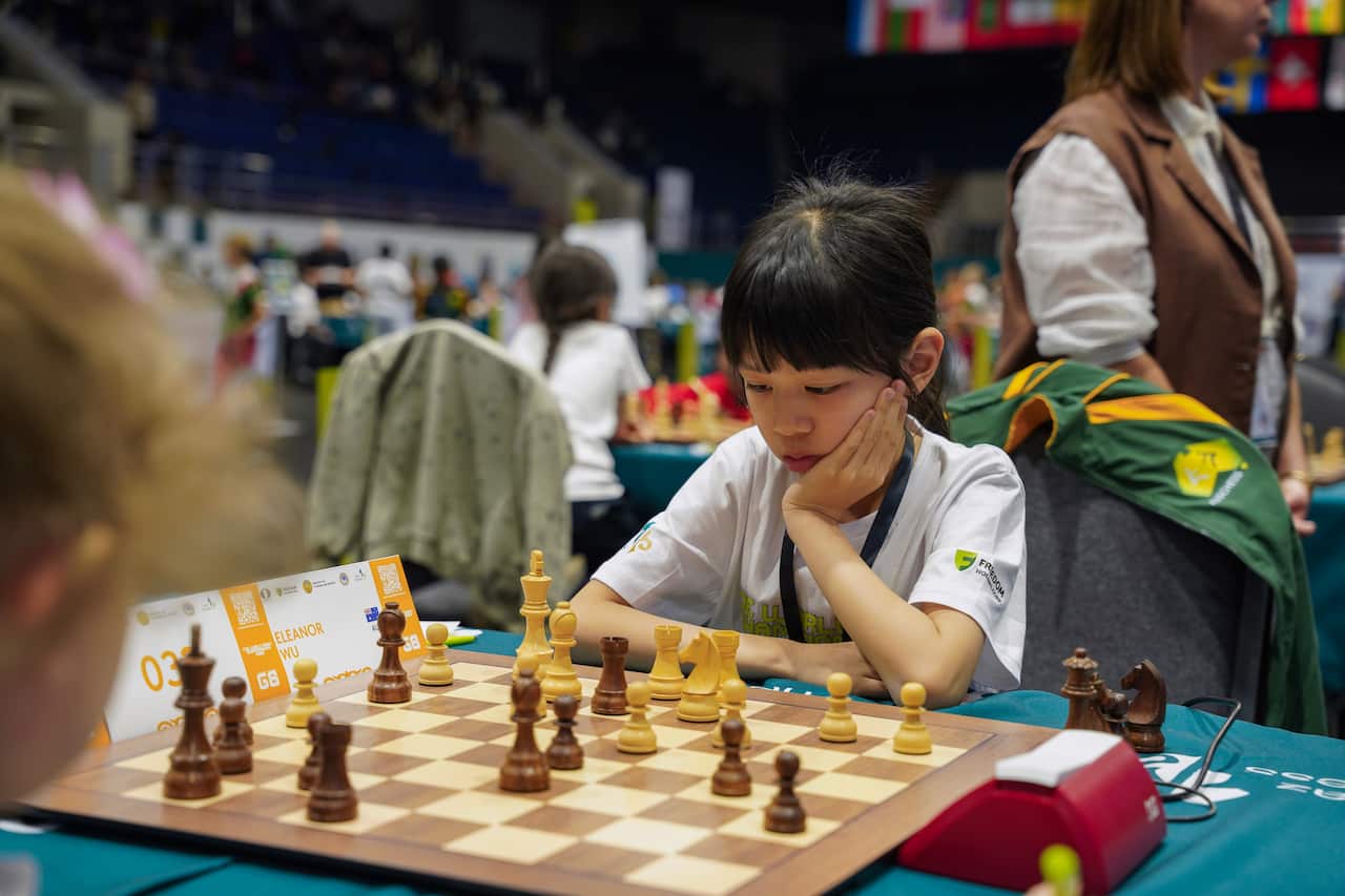 A young girl, her palm over her cheek and a sombre expression, is playing chess.