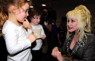 Dolly Parton, wearing a black dress, speaks to two children.