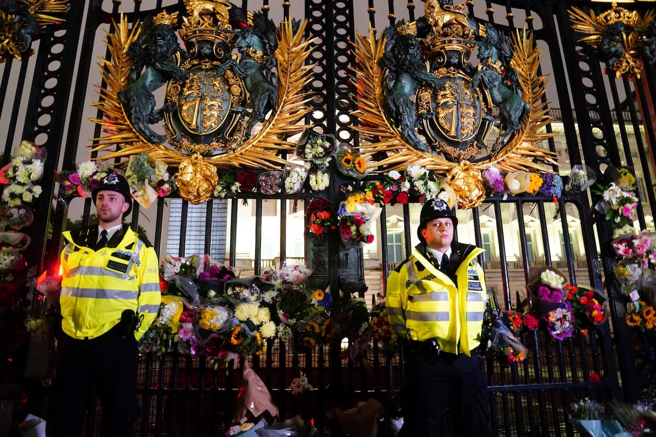 Guards stand at Buckingham Palace surrounded by flowers 