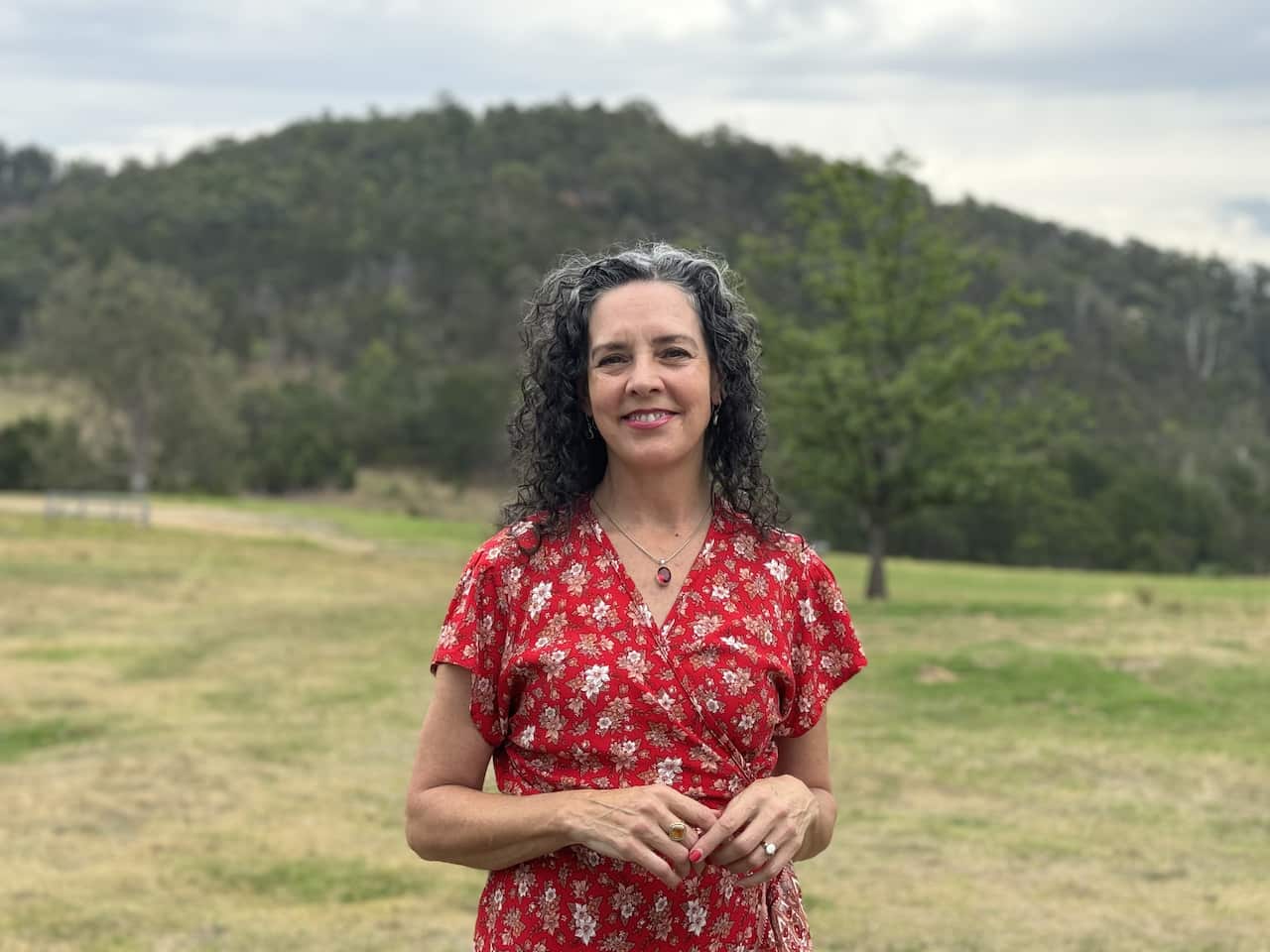 A woman in a red dress smiles as she stands in a field.
