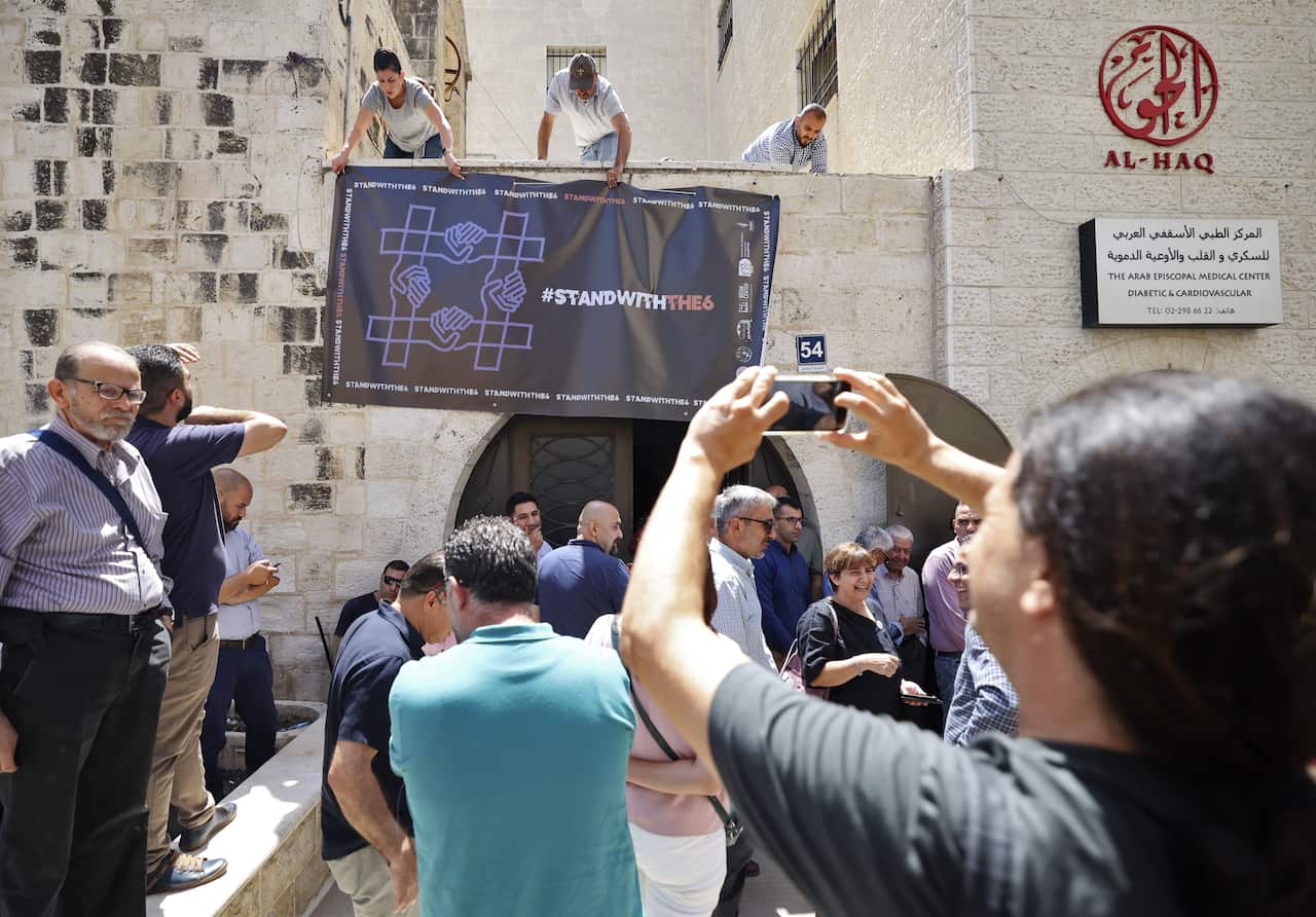 Activists hang a banner outside a stone building. People gather in front.