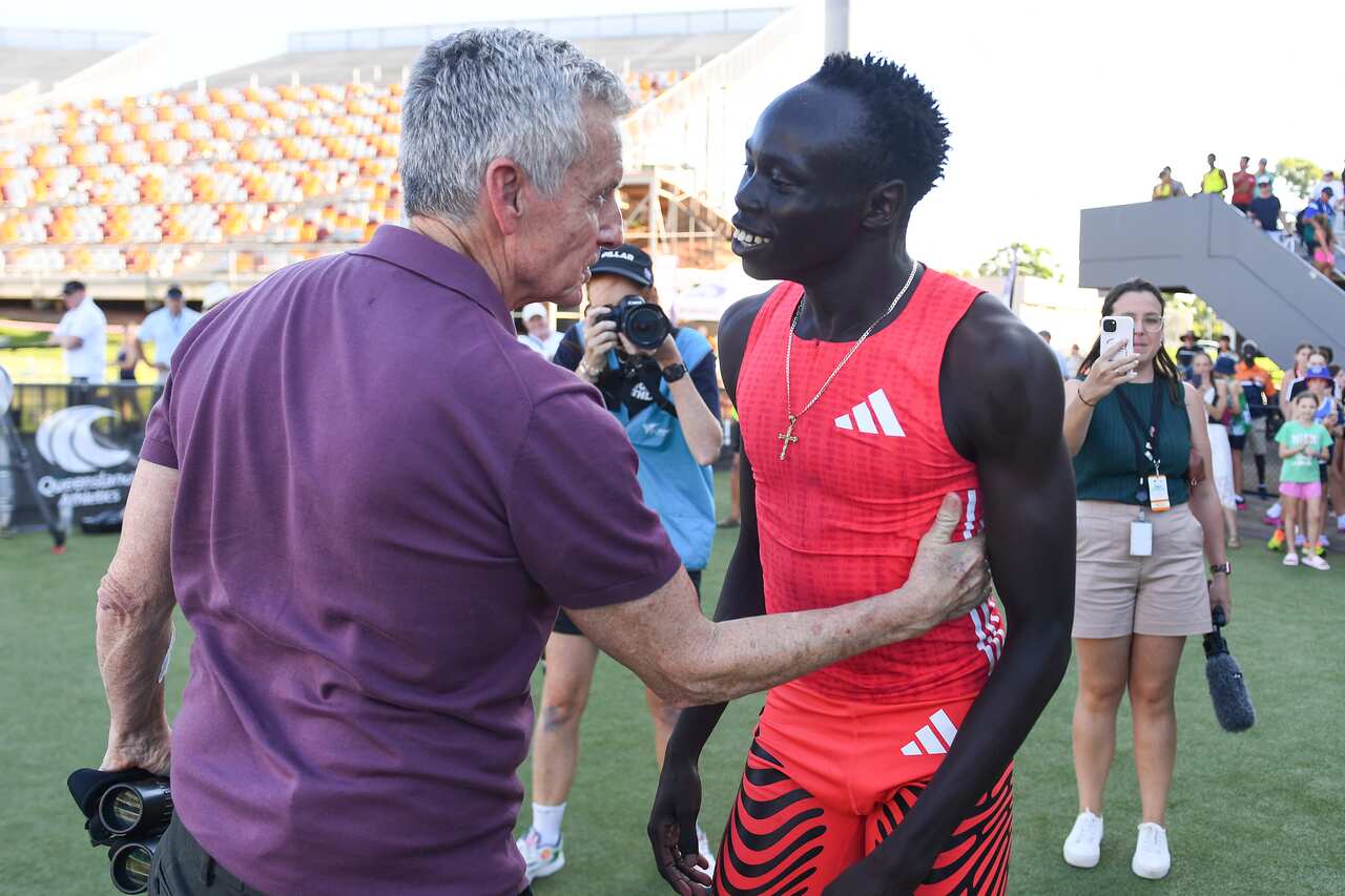 A man in a purple shirt hugs a younger man in red athletics clothing