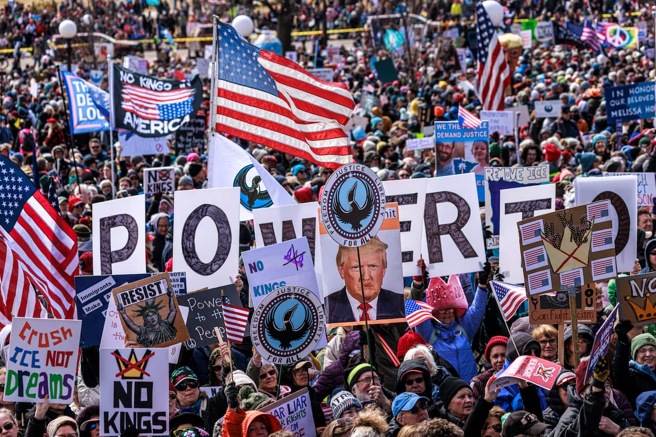 People hold signs and flags as a large crowd gathers outside a city hall