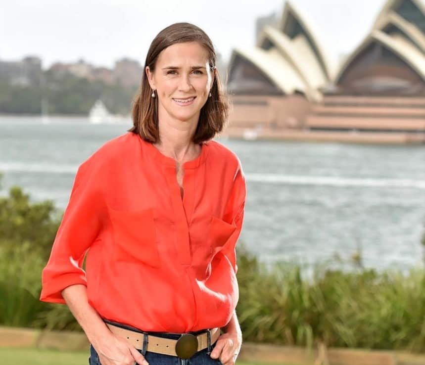 A woman in an orange shirt stands in front of Sydney Harbour. 