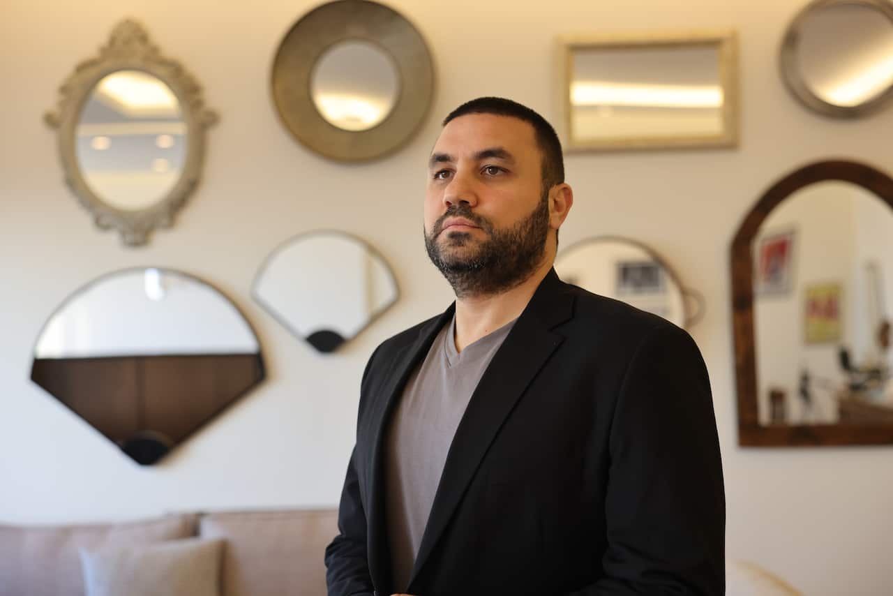 A bearded man in a black blazer over a gray shirt poses for a photo