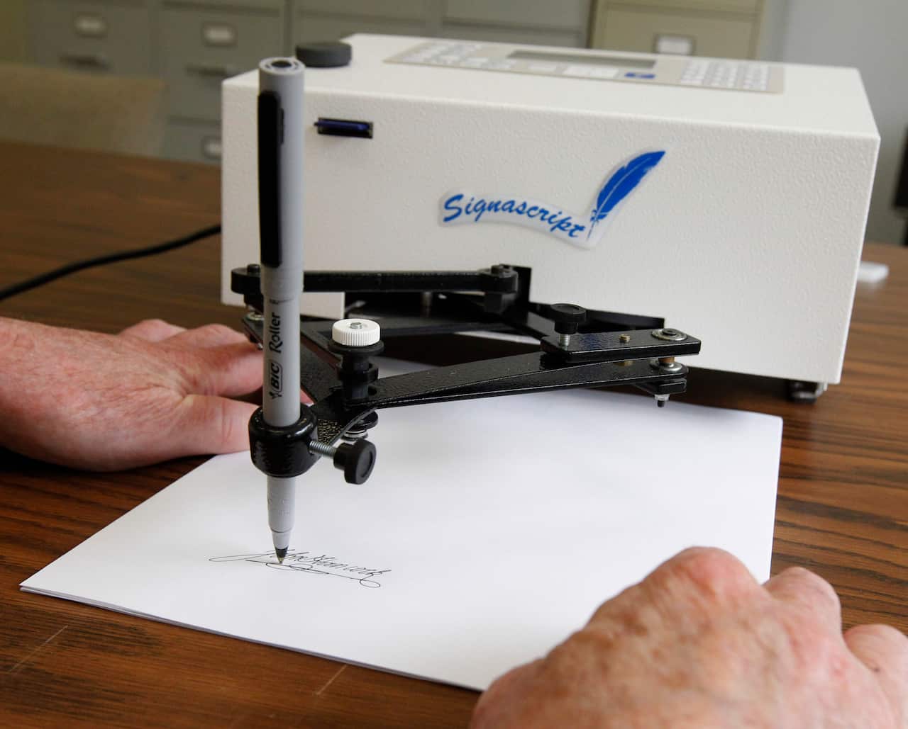 A mechanical device operating a pen and signing someone's signature on a piece of paper