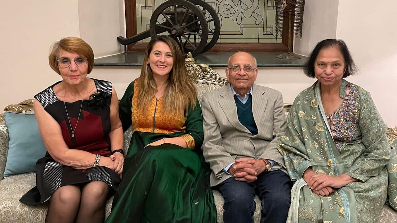 An older woman, a middle-aged woman, an older man, and another older woman in formal attire pose together smiling on an ornate couch.