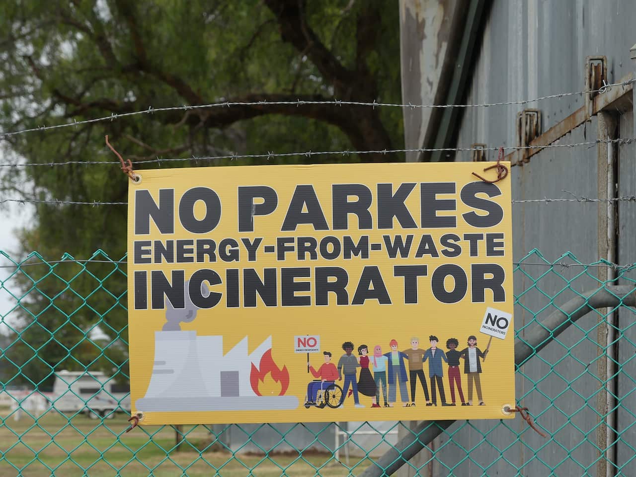 A sign protesting a proposed energy-from-waste facility is seen secured to a wire fence.