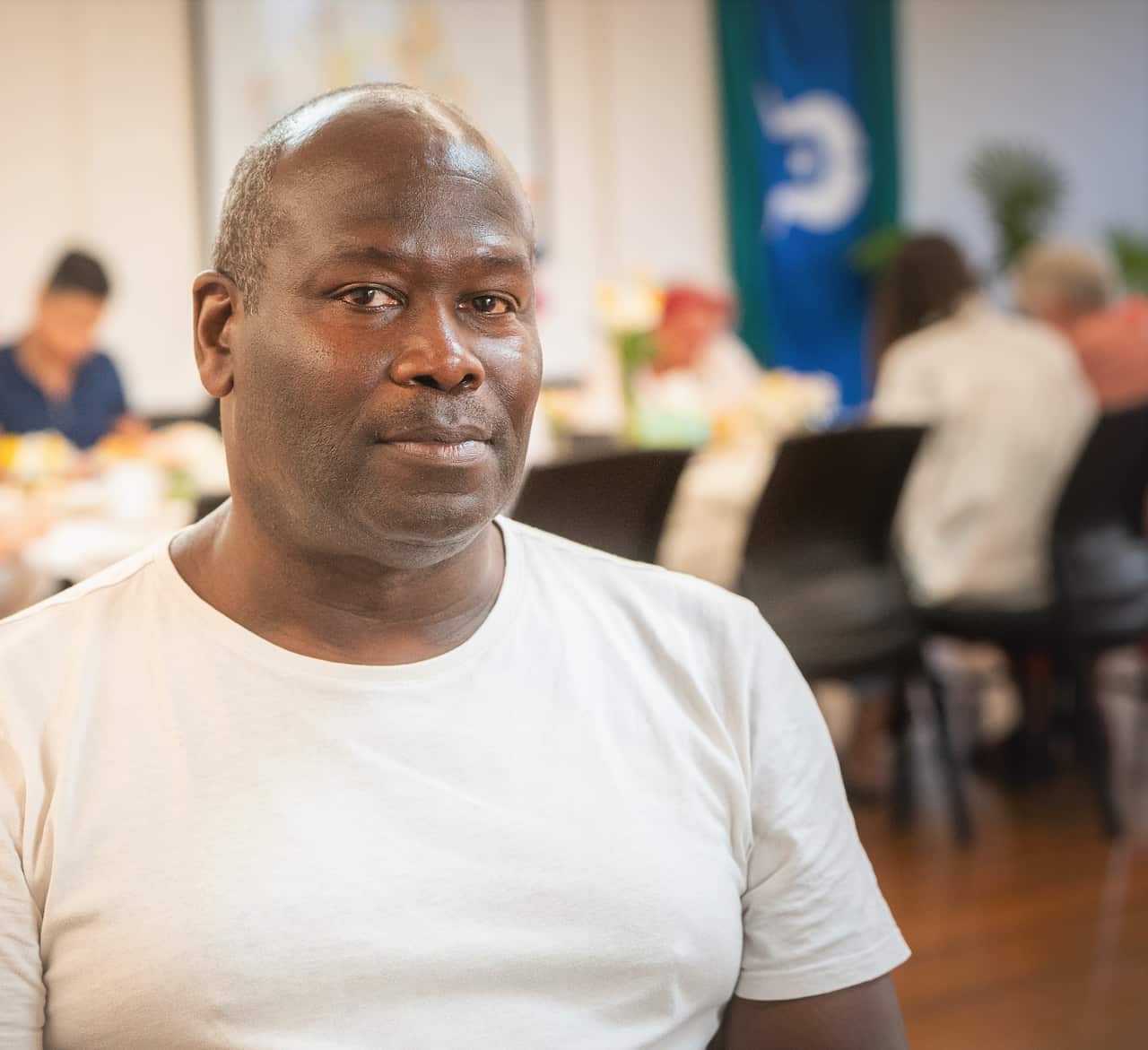 A man in a white T-shirt in front of a table full of people.