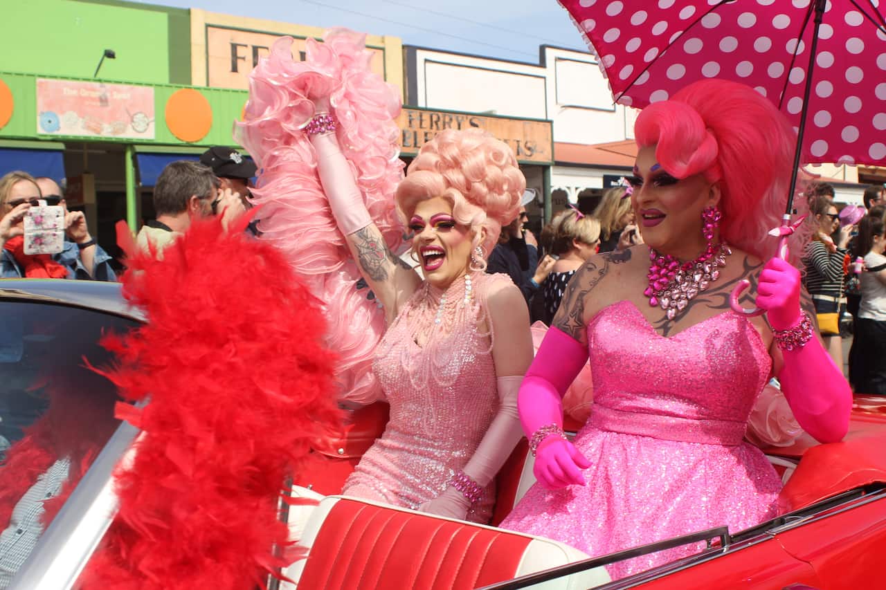 Two people dressed in bright pink drag sitting in the back of a car for the annual parade.