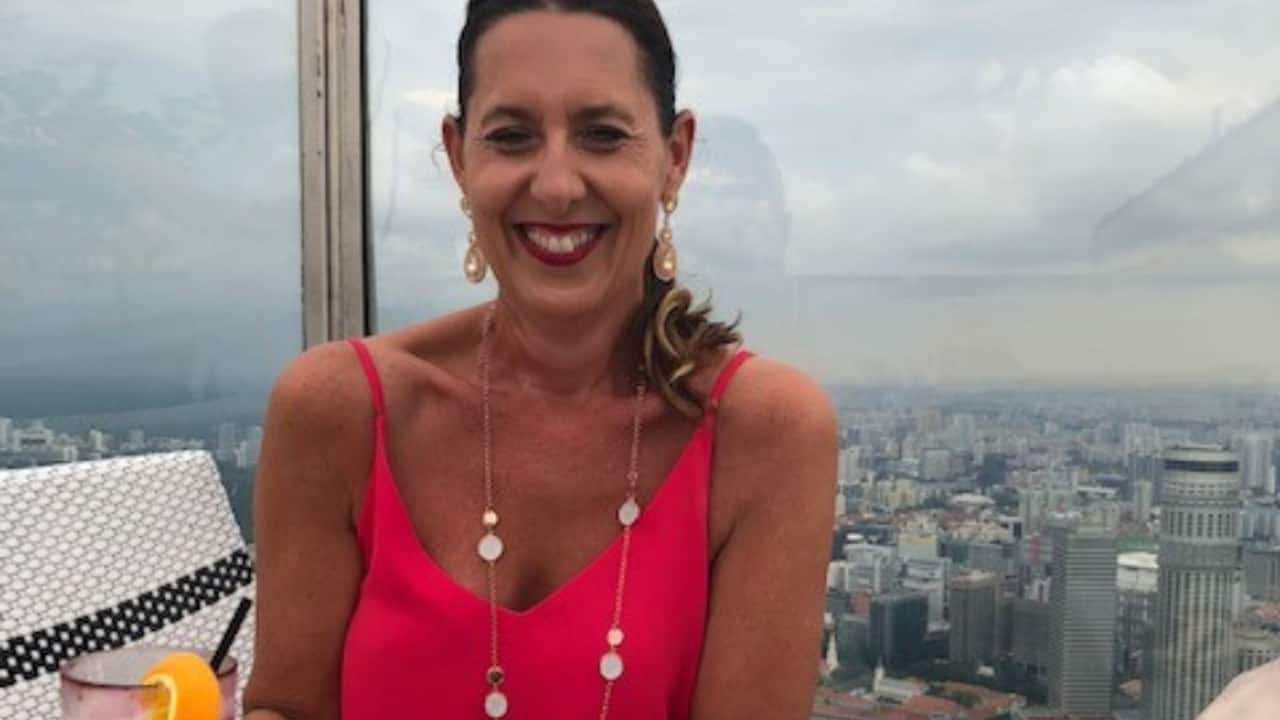 a middle aged woman drinking a cocktail on a rooftop bar in a city