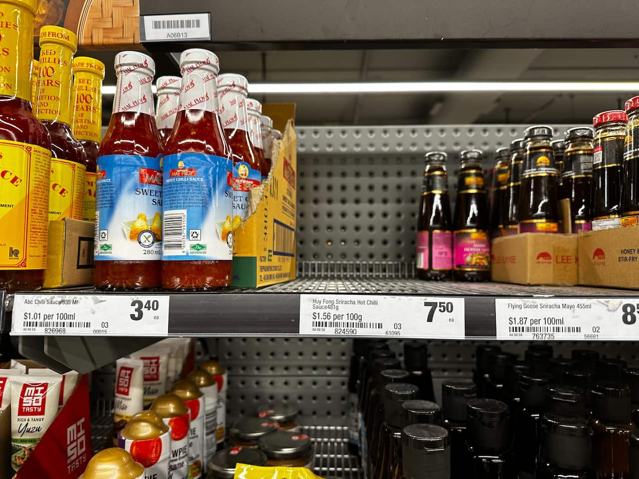 Supermarket shelves with chilli sauce bottles. There is an empty section where products are out of stock.