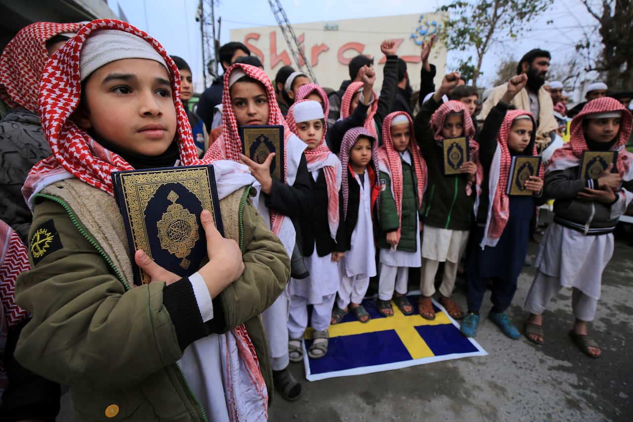 Children holding Korans standing outside. Some are standing on a Swedish flag.
