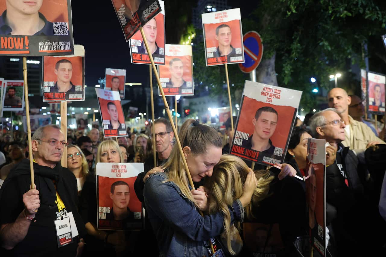 Women embrace as they join people holding pictures of hostages.