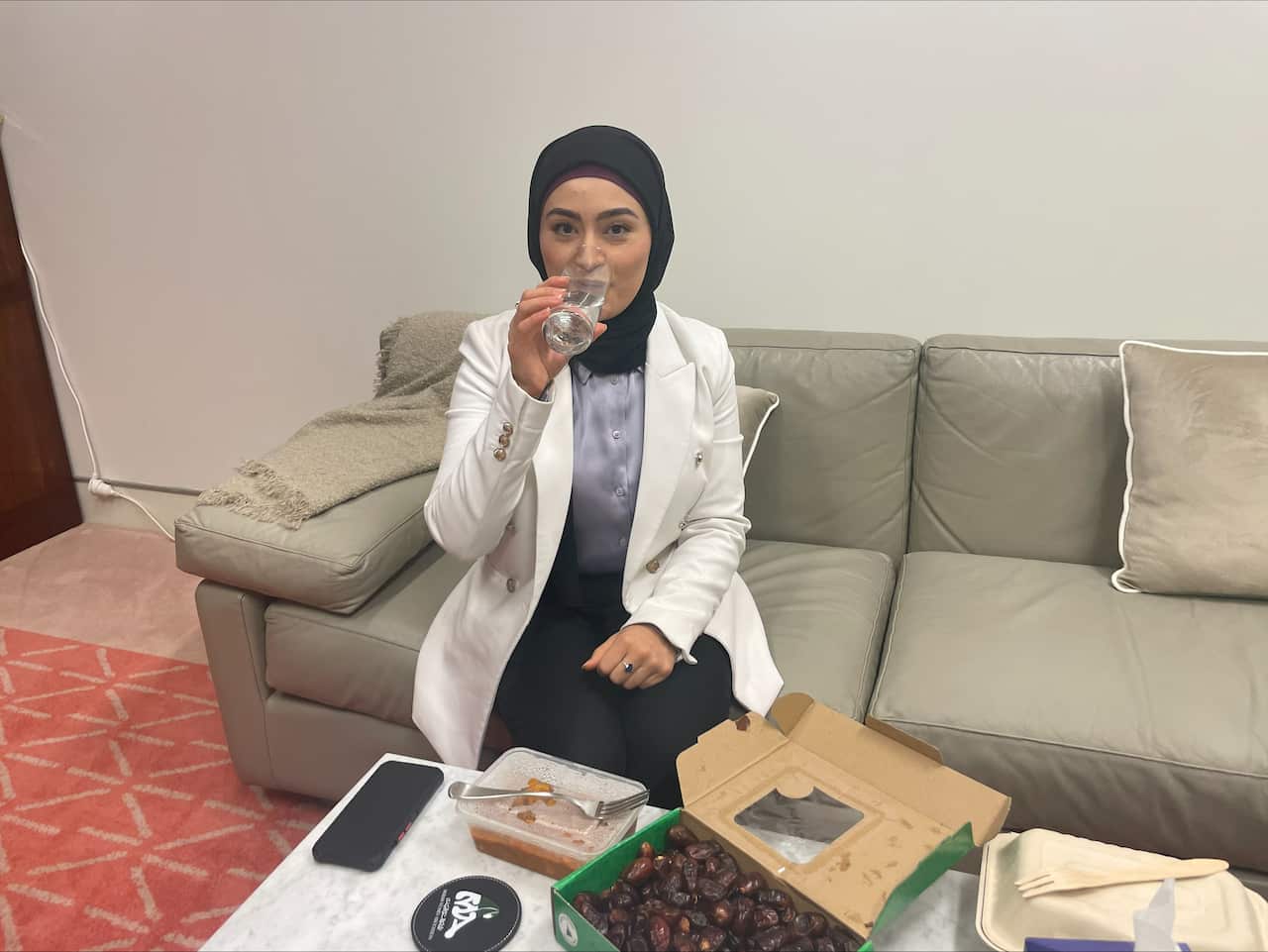 Fatima Payman drinks from a glass of water on a couch.