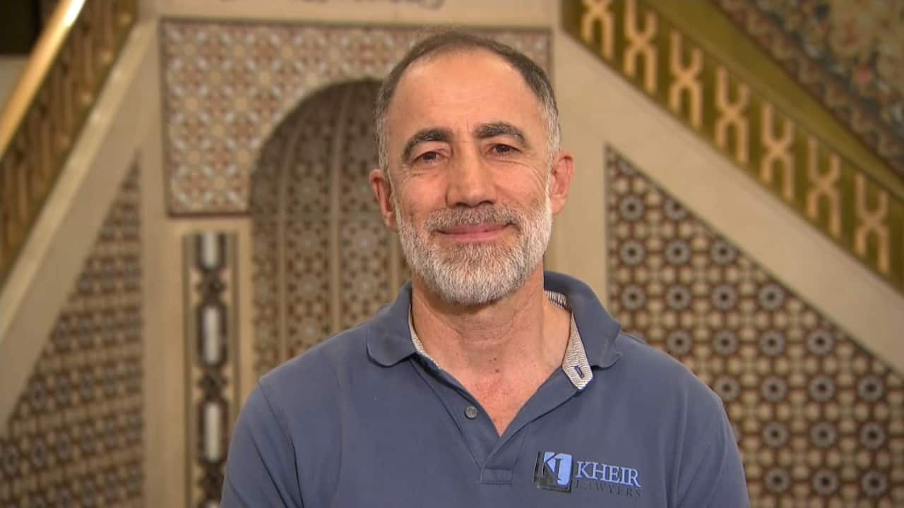 A man in a blue polo shirt is standing inside a mosque.