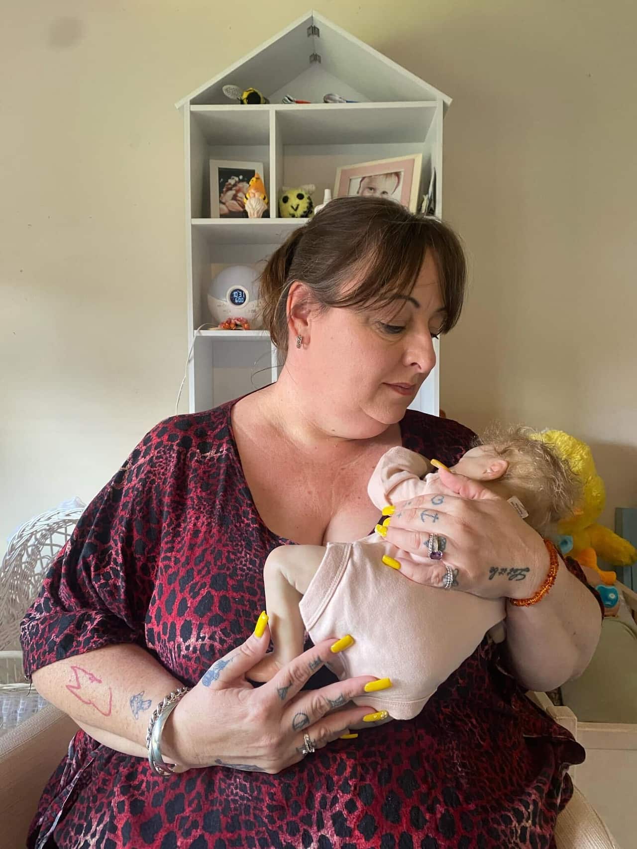 A woman in a red leopard print dress cuddles a realistic baby doll against her chest