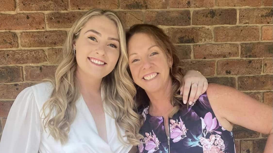 Two women standing against a brick wall smiling