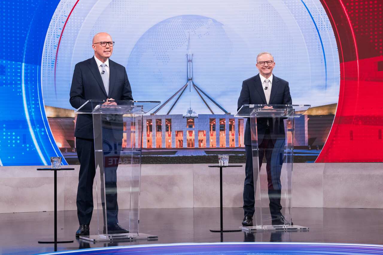 Peter Dutton and Anthony Albanese smile as they stand at separate lecterns. 