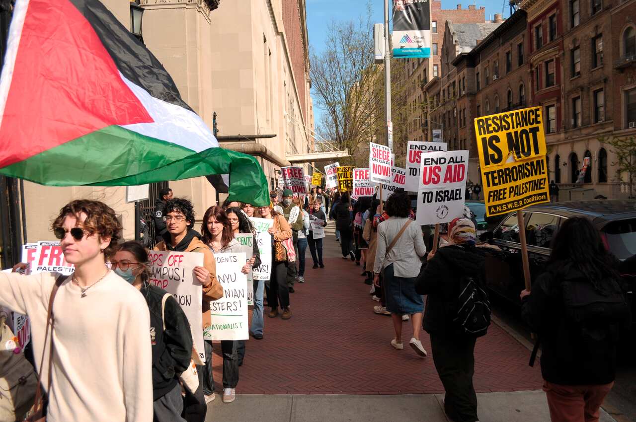 Student protesters at Columbia University march in a line carrying placards and Palestinian flags