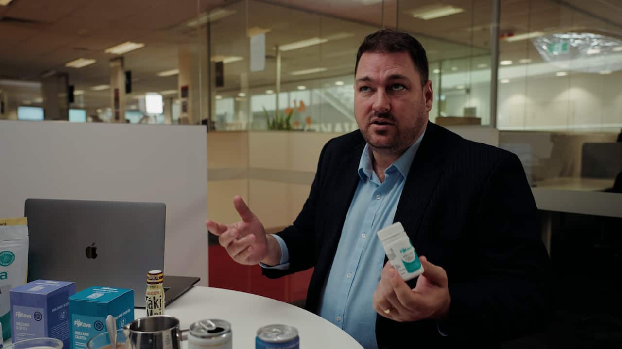 A man holding a container containing kava pills.