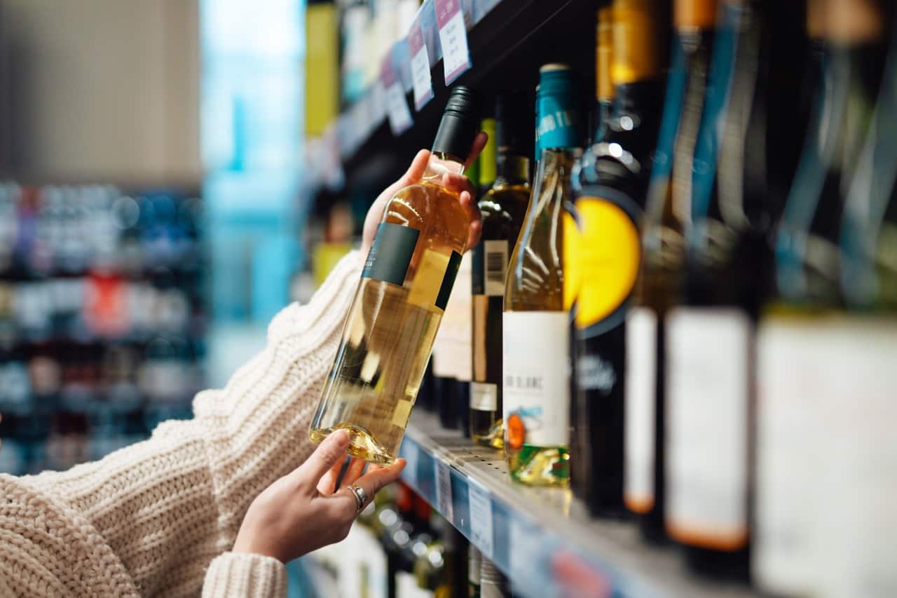 A person holding a bottle of white wine in a supermarket.