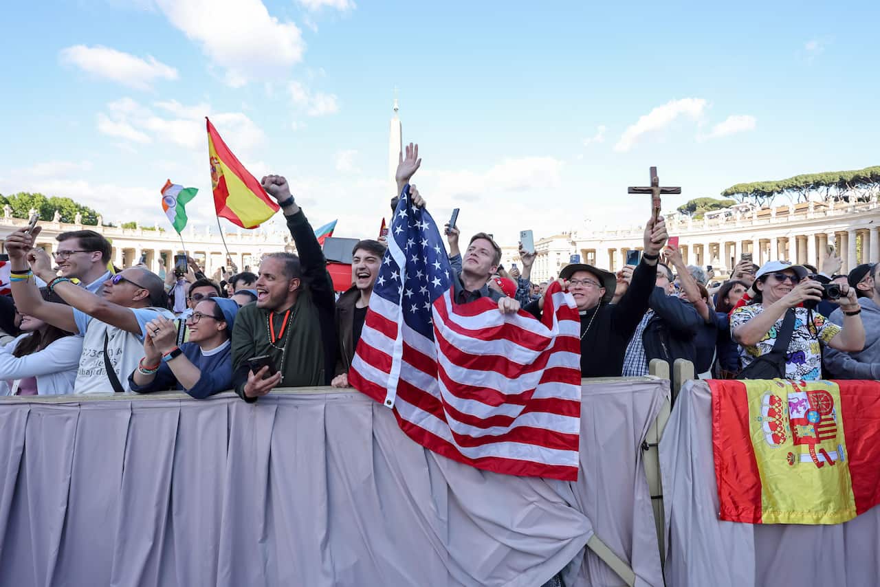 People hold up a US flag and a crucifix at the front of a cheering crowd.