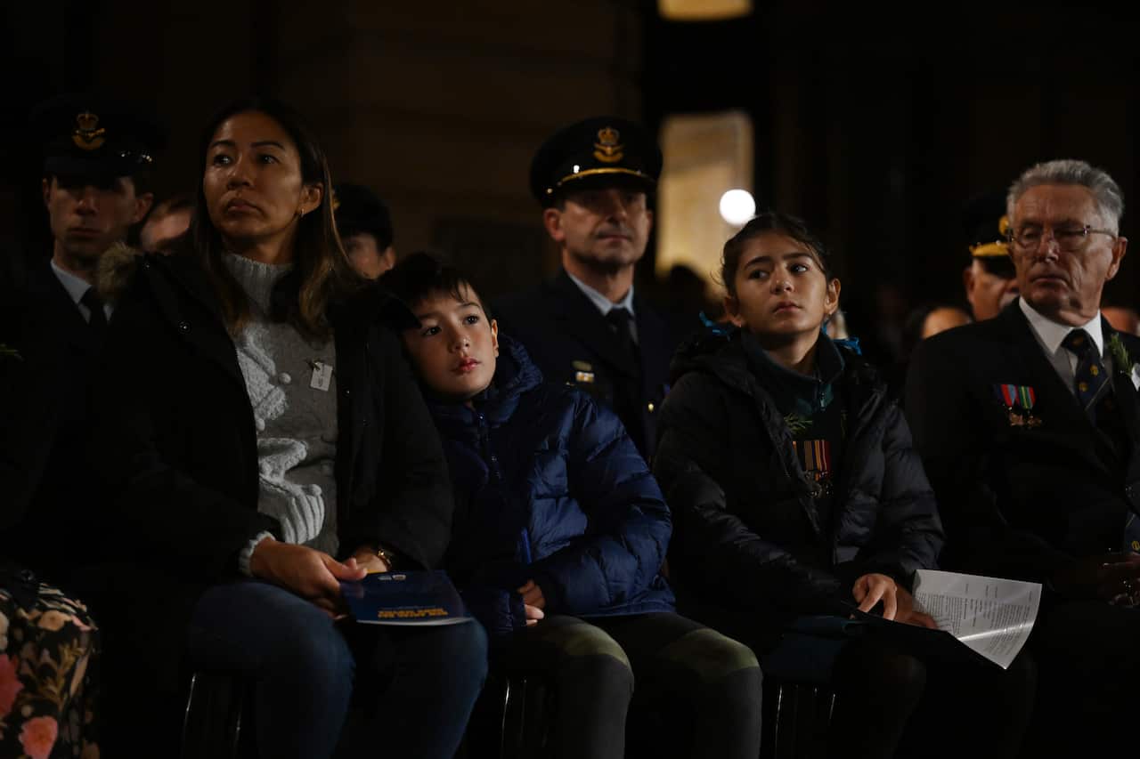 Several people, some of whom are wearing military medals, sit in the dark.