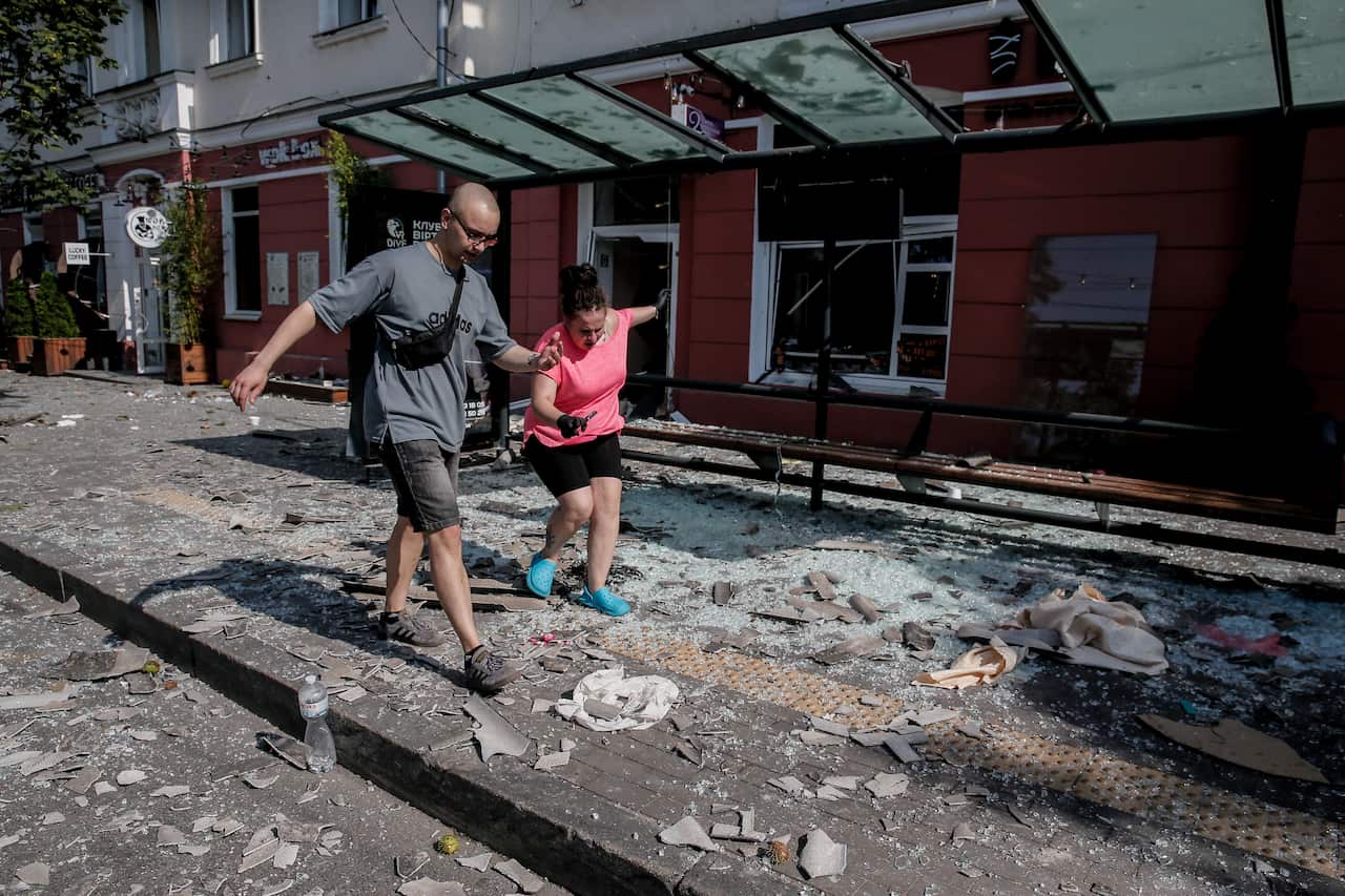 Two people walk over debris in a street after a missile attack.