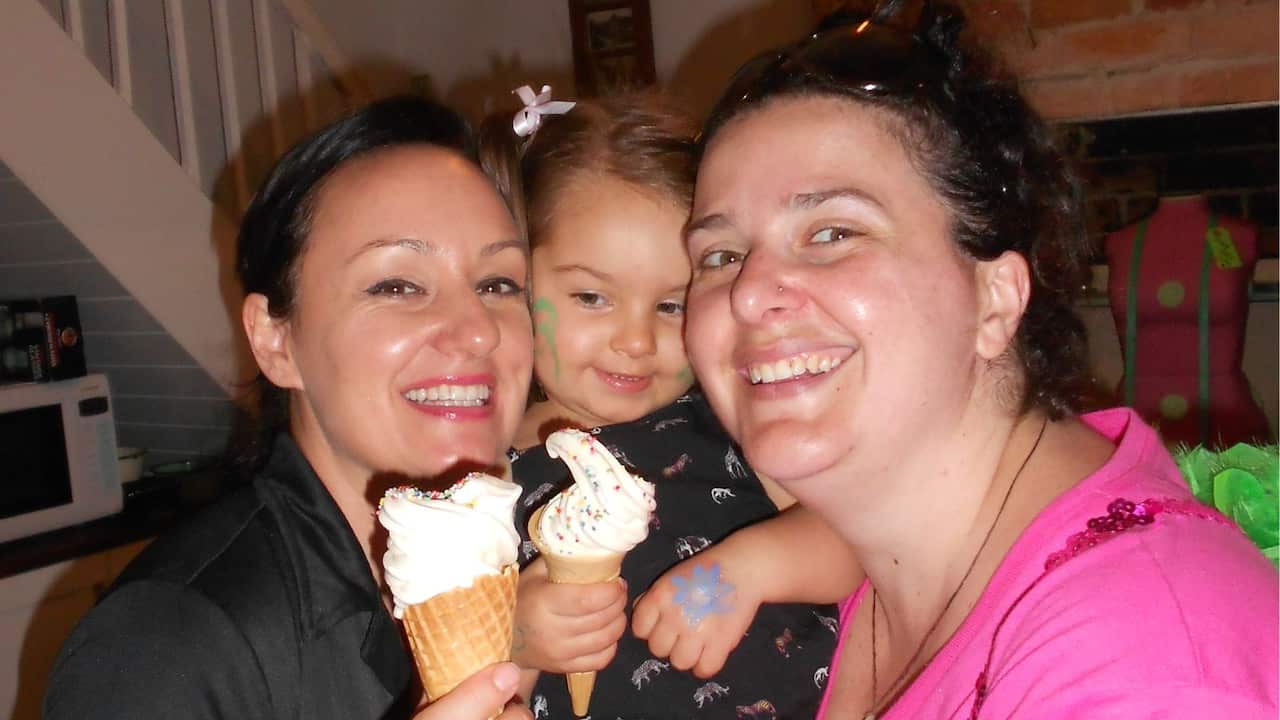 two women with dark hair smiling holding a toddler between them and holding an ice cream cone