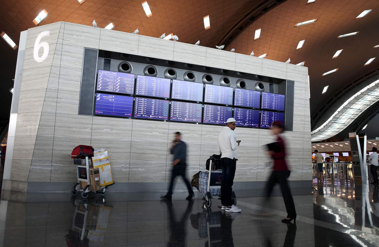 People walking past a departures board at an airport.