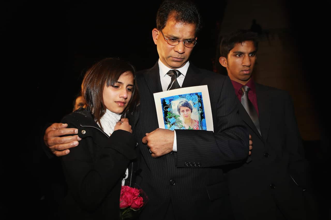 Jacinta Saldanha's daughter Lisha hugs her father Ben Barvoza who is holding a photo of his late wife. Jacinta Saldanha's son Junal stands beside them. 