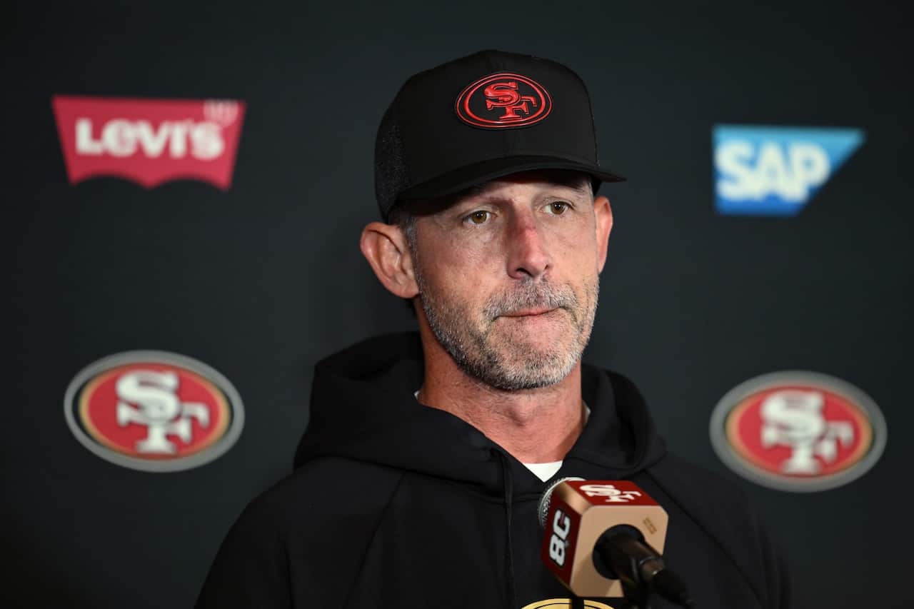 A man wearing a black top and black cap with red SF logo speaks into a microphone