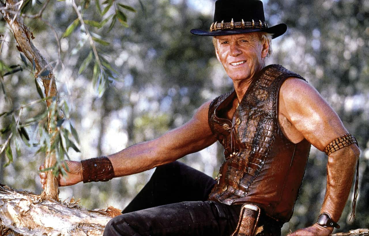 Paul Hogan dressed in pants, a crocodile skin vest and a wide brim hat.
