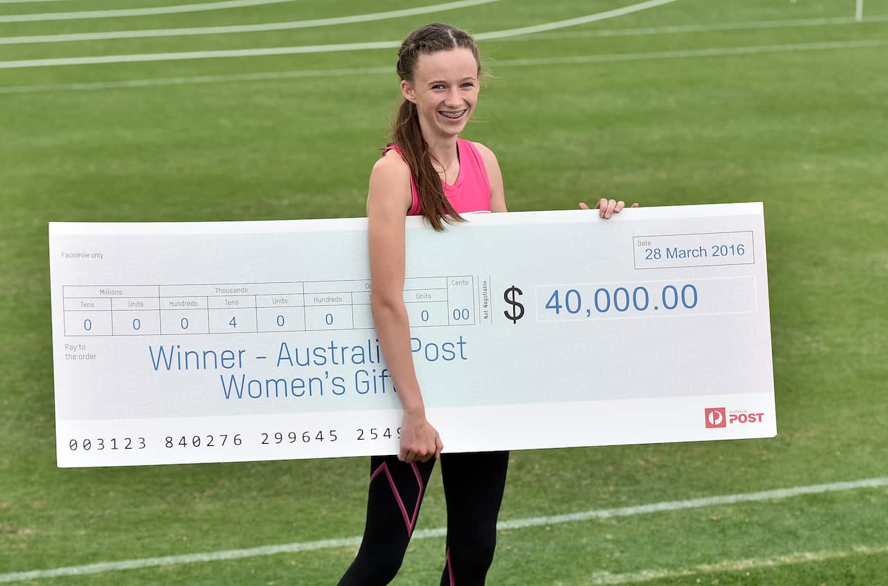 A woman holding a large novelty cheque on a sports field.