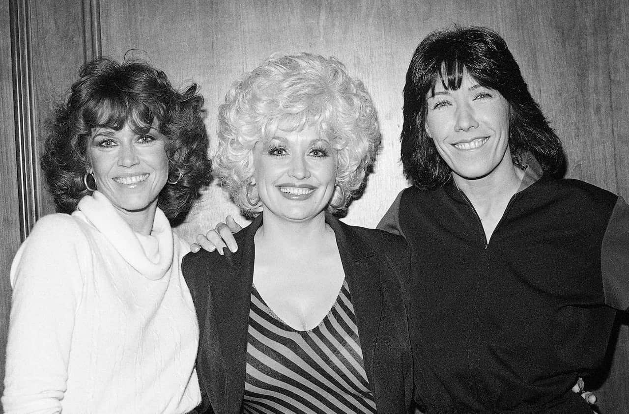 Jane Fonda, Dolly Parton and Lily Tomlin standing next to each other and smiling.