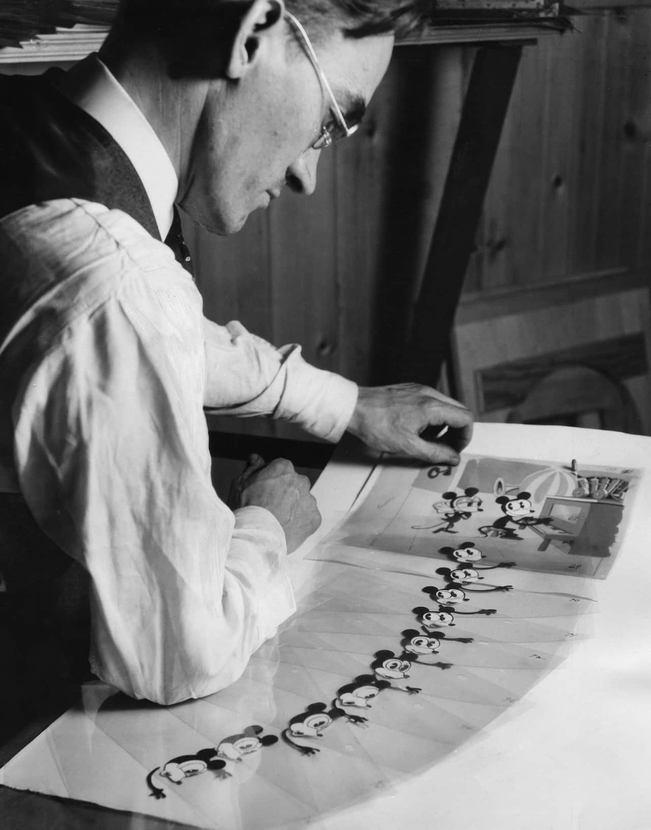 A man creating a Mickey Mouse cartoon motion picture, with many drawings of the character on the table.