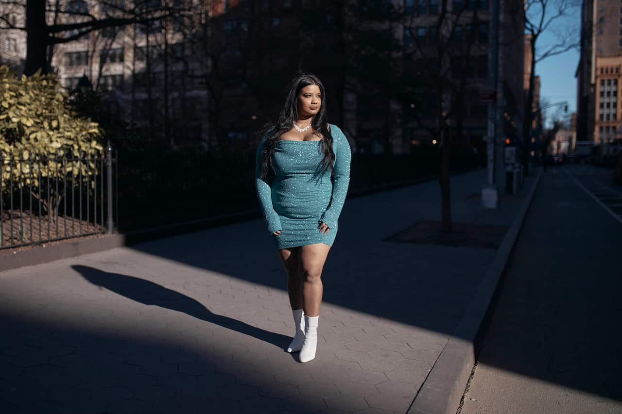 A young woman wearing white boots and a sparkly dress standing on a footpath