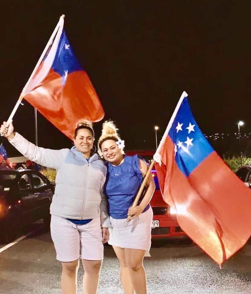 Two women stand holding Samoan flags.