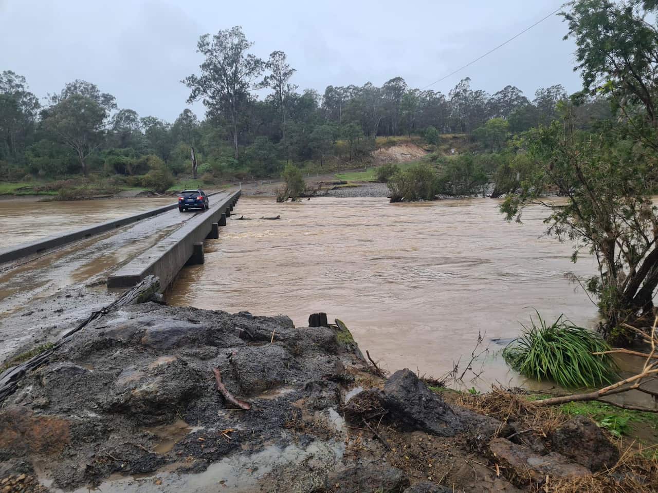 A car is passing through a bridge over a flooded river.