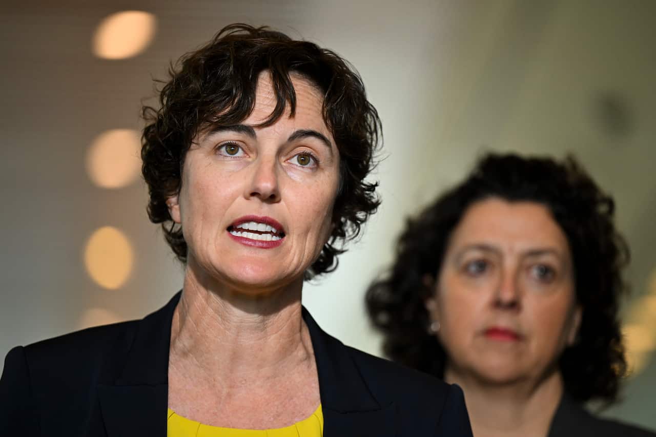 Woman in black blazer and yellow shirt speaks.