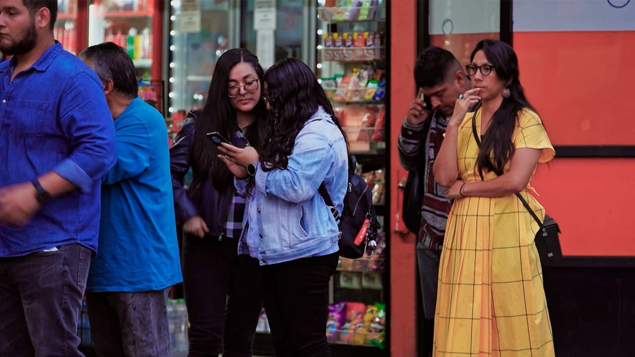 A woman wearing a yellow dress and a crossbody long-strapped handbag is standing in line in front of two women and two men. There are vending machines visible in the background